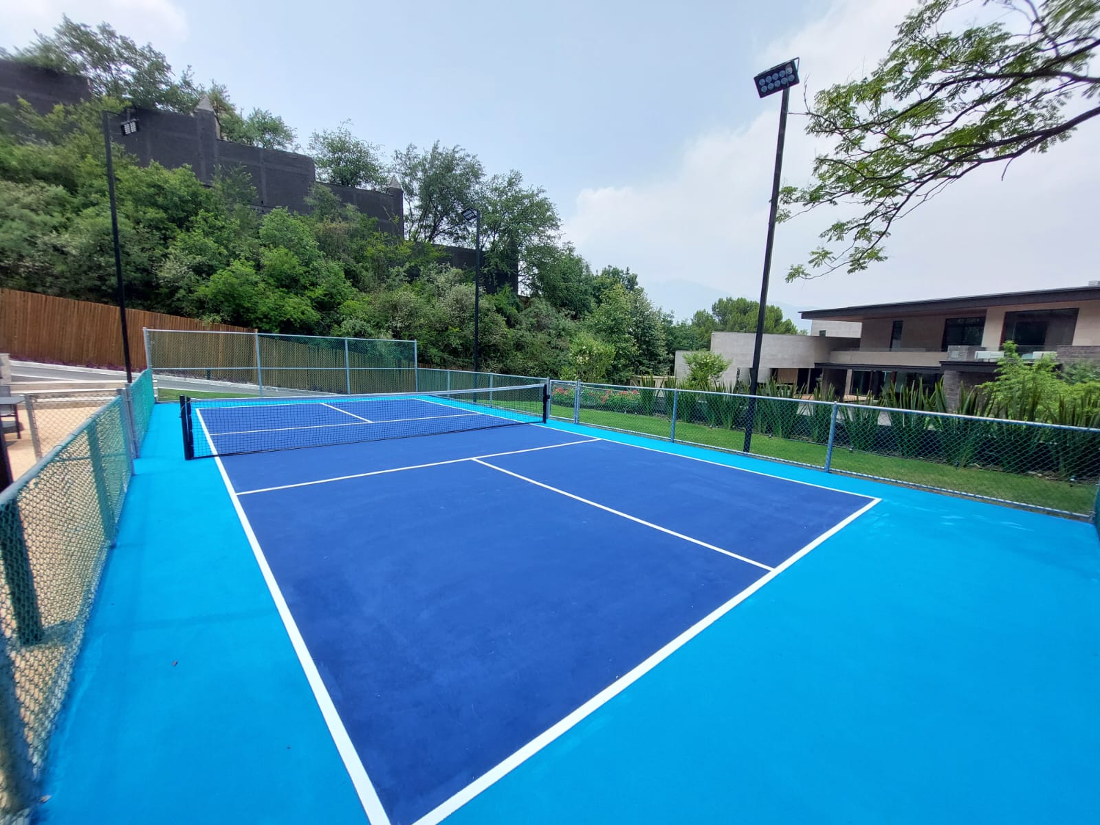 Cancha de pickleball residencial construida por CanchasdePickleball.mx en casa particular de Monterrey con pintura azul Laykold y LED